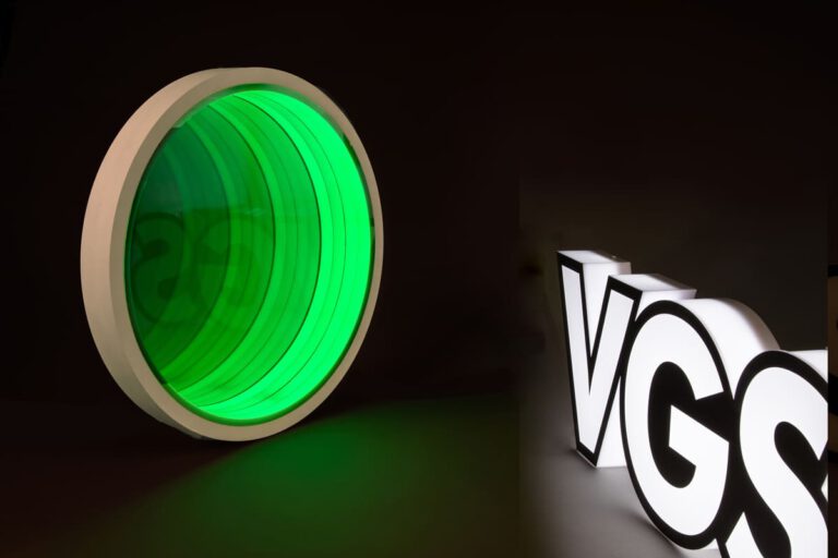 Grüner Zylinder mit unendlichen Spieglungen links, VGS-Logo leuchtend in Weiß rechts