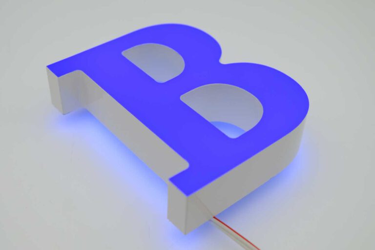 Zu sehen ist ein LED-Leuchtbuchstabe in Form eines "B" von Maxxluxx. Die Frontseite ist mit einer blauen, transluzenten Farbfolie überzogen, während die Rückseite ein sanftes hellblaues Licht ausstrahlt. Die Seiten sind lichtdicht lackiert und in Weiß gehalten. Dieser kombinierte Front- und Rückleuchter bietet eine große Farbvielfalt und kann ganz nach Kundenwunsch individuell gestaltet werden.